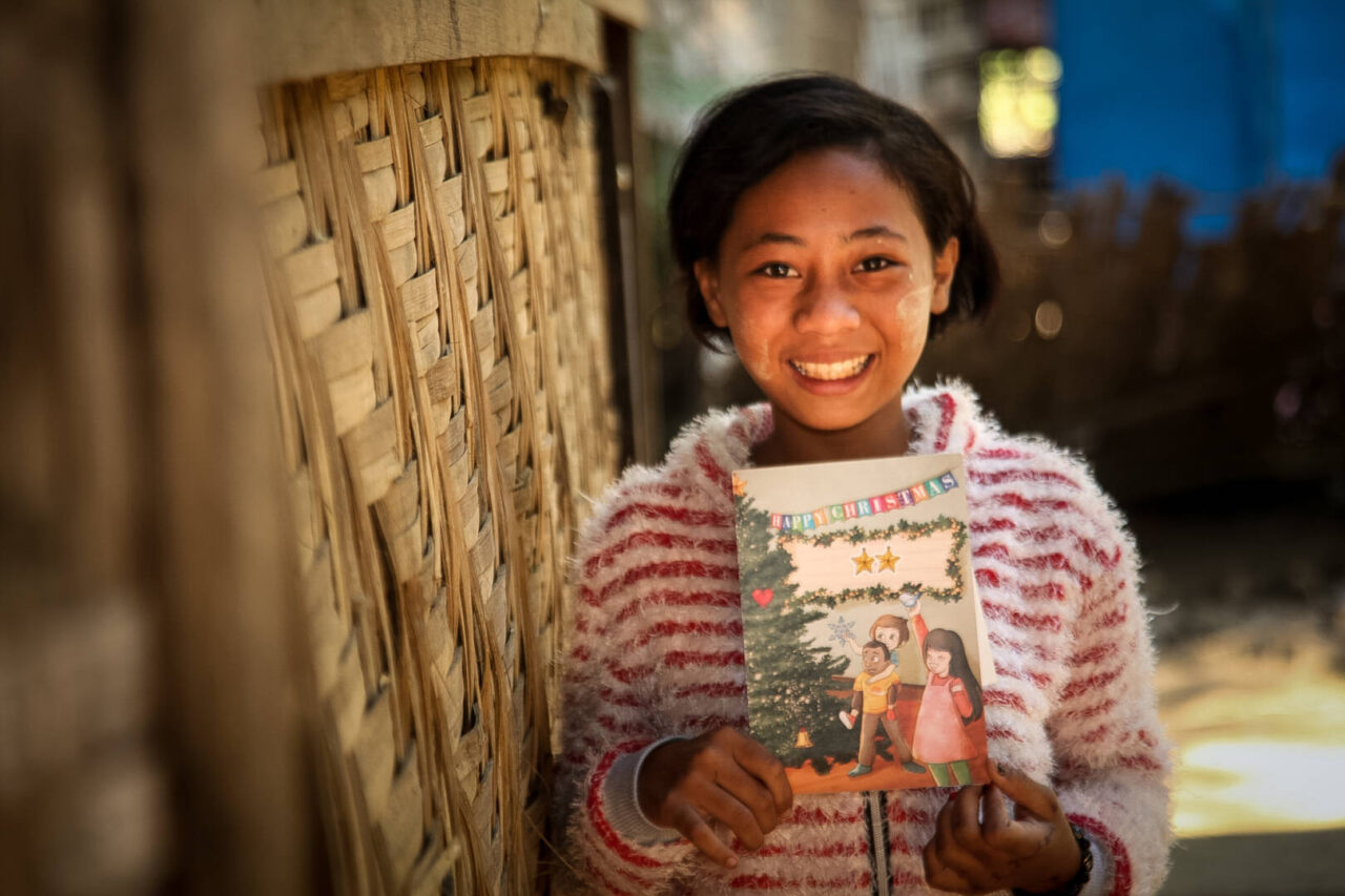 A girl smiles at the camera while holding up a Christmas card.