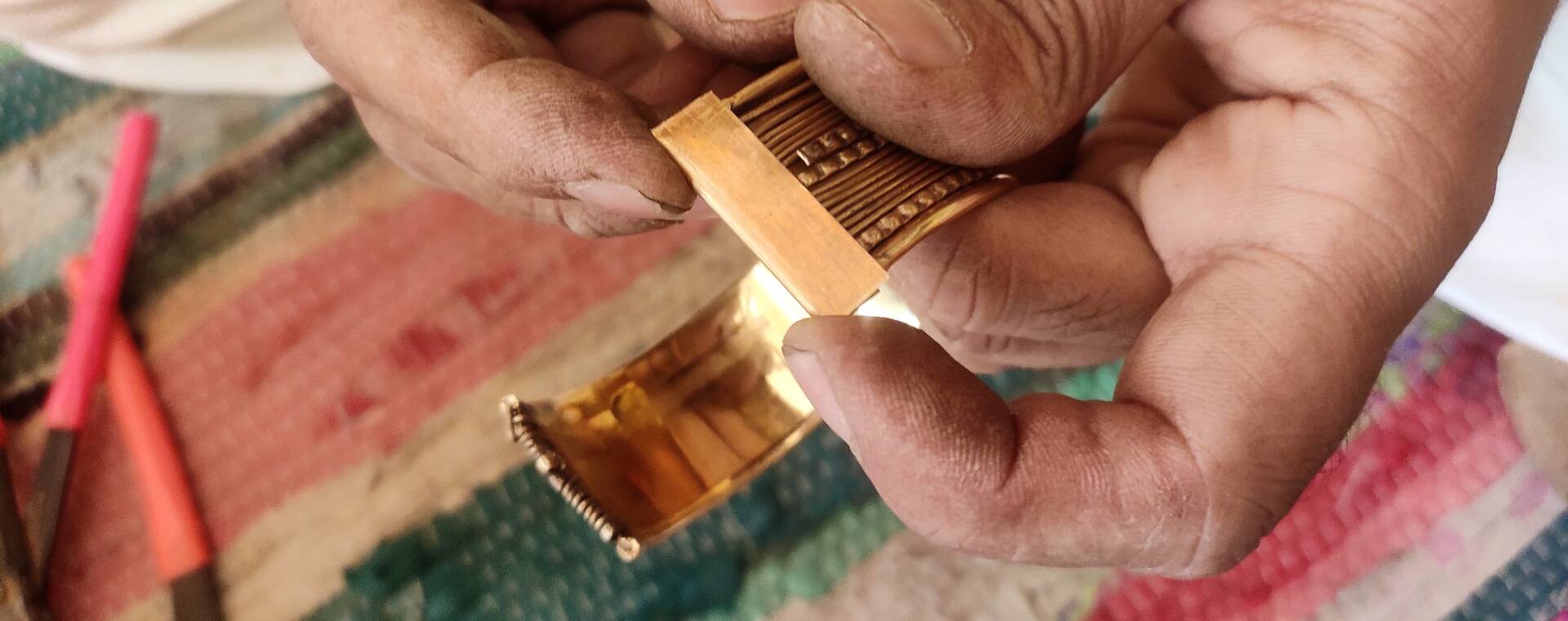 A close-up of two hands holding a brass bracelet.