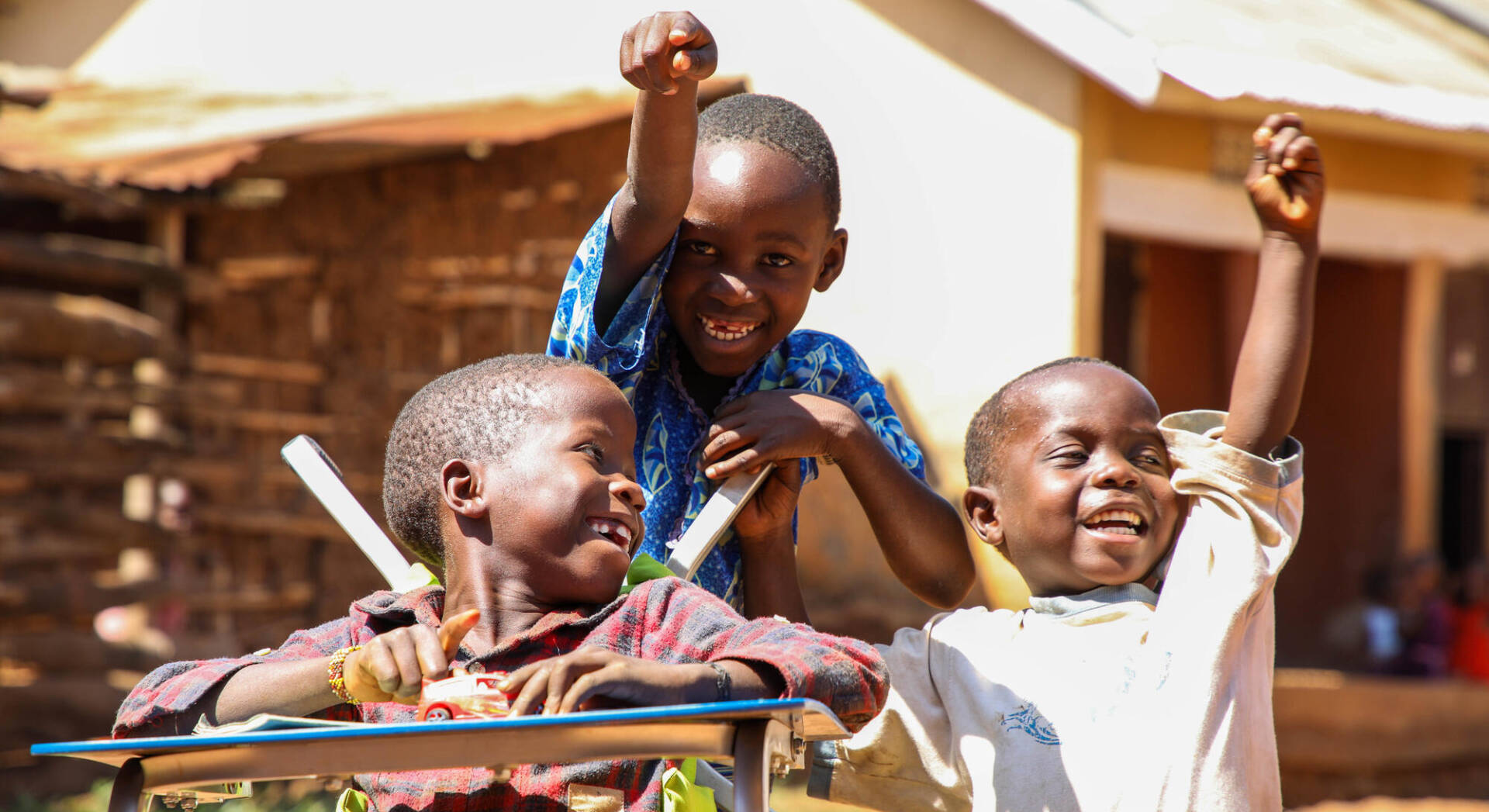 Isma sits in his wheelchair looking back to two friends who throw their hands up with excitement