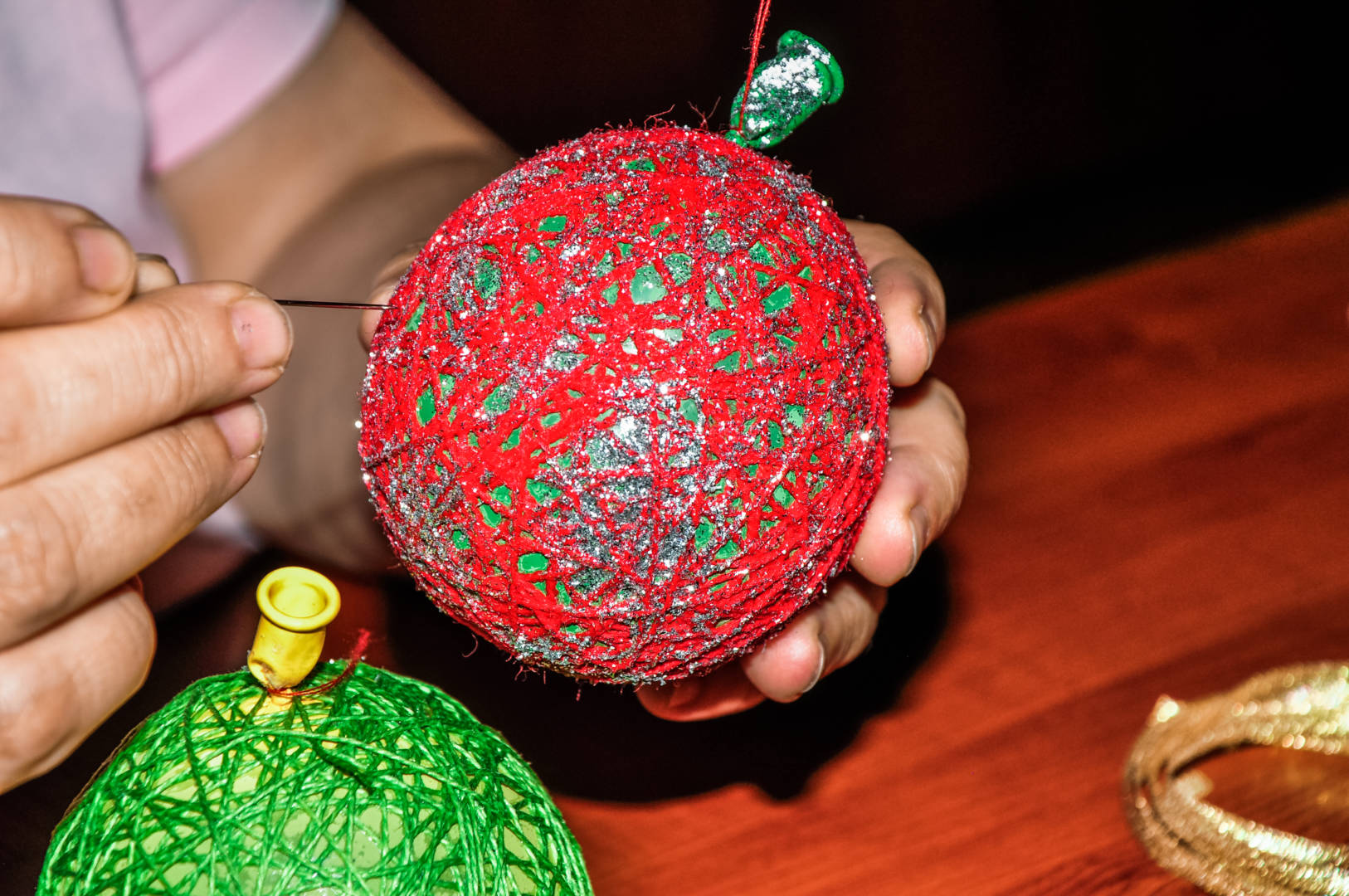 Hands work on an ornament made from a balloon and yarn.