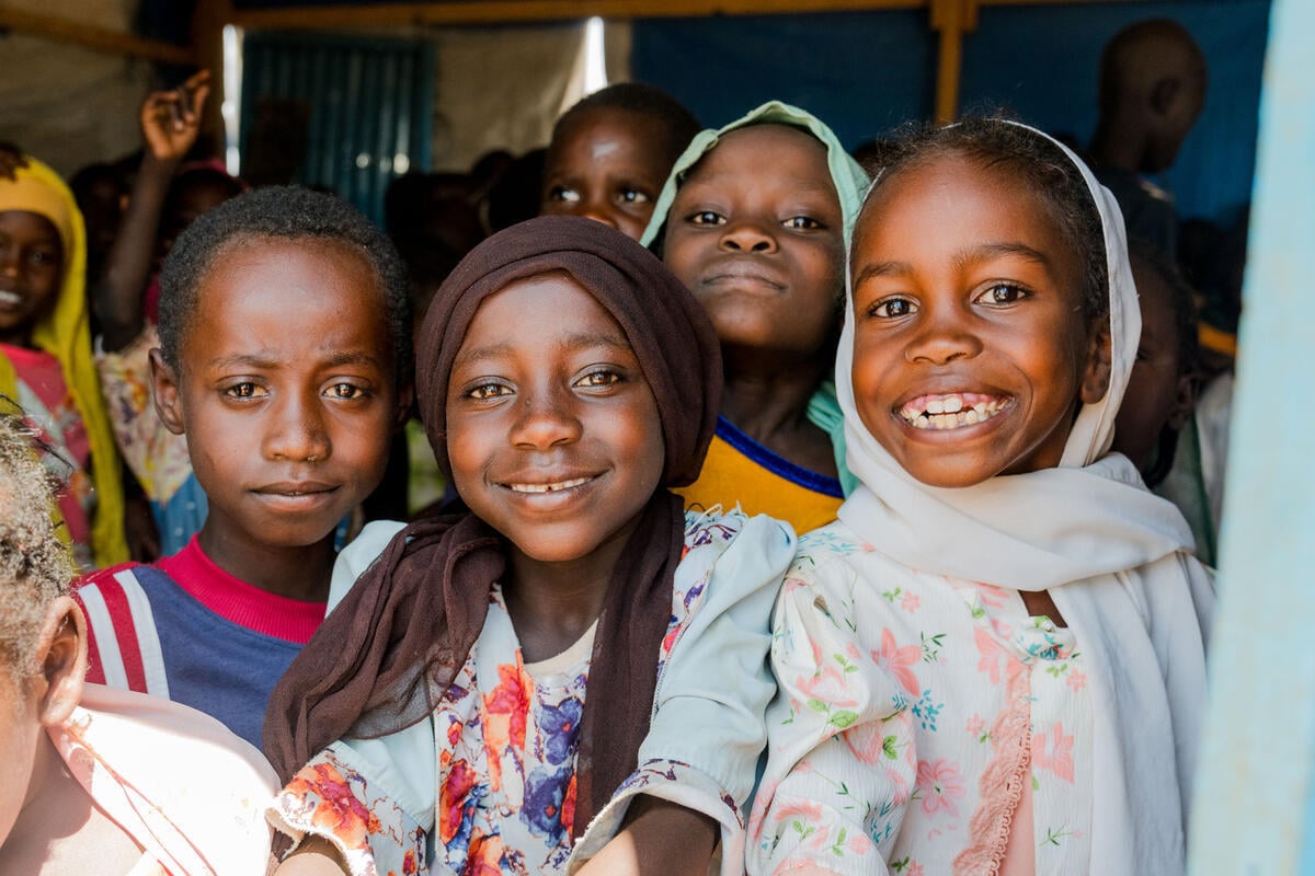 A group of children in Chad, many wearing headscarves, smile and look toward the camera.