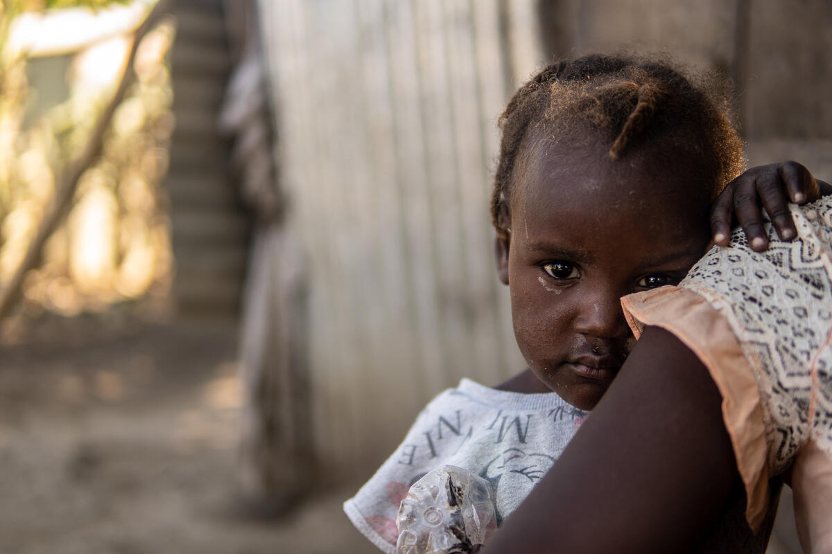 A young girl looks over her mother&rsquo;s shoulder and into the camera.