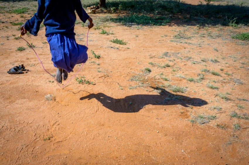 A schoolgirl jumps over rope, casting a shadow on the ground below.