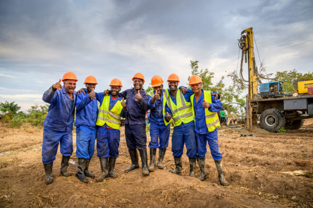 Seven water drillers give the thumbs up sign as they prepare to drill for clean water in central Malawi. Spend a day with a drill crew in Malawi that works 90% of the year on the road, away from their families. They cook their own food. They wash their own clothes, always covered mud after a long day at work. They live in tents and sit on overturned buckets instead of on chairs. And yet, they wouldn&rsquo;t have it any other way.