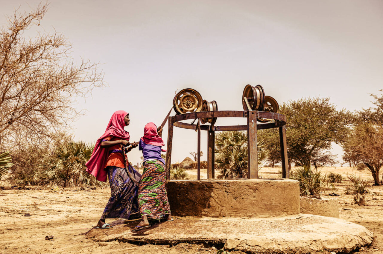 Two girls in Niger collect dirty water from an open well Two girls wearing pink head scarves pull ropes to draw water from an open well.
