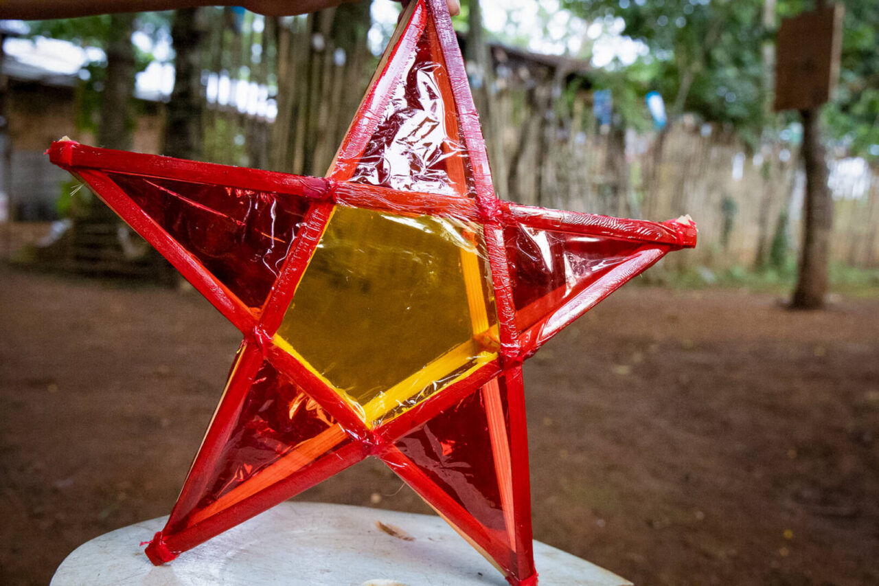 A Filipino father and daughter tie sticks together to make a star, then decorate it with colorful clear plastic paper.