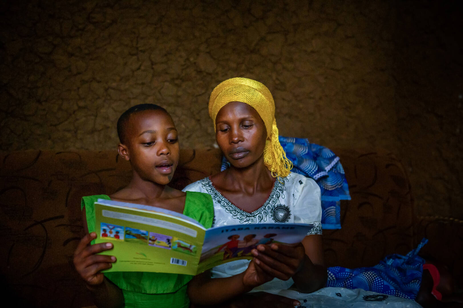 Keza_reading Dativa listens to Keza read a book that came from the World Vision’s reading camp Keza attends.