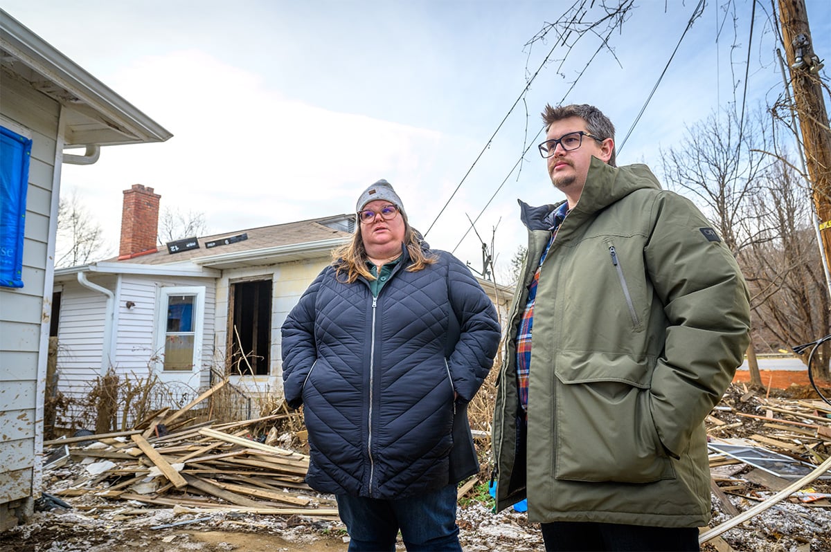 two people stand in front of their destroyed home