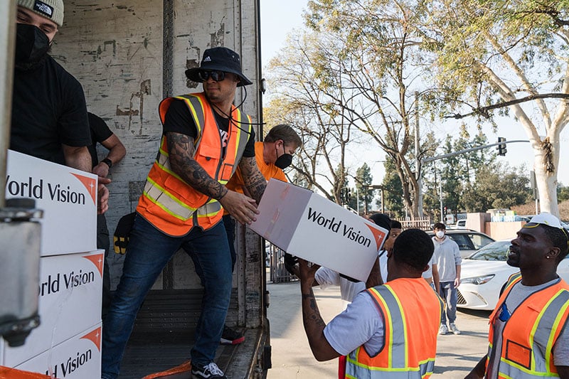 Men wearing orange vests pass white World Vision boxes to each other to move them off of a truck.