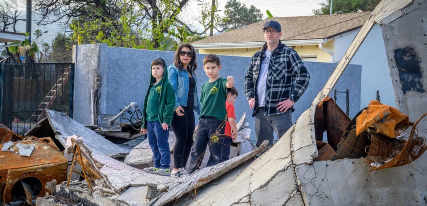 A man, woman, and three boys stand in front of rubble of a home.