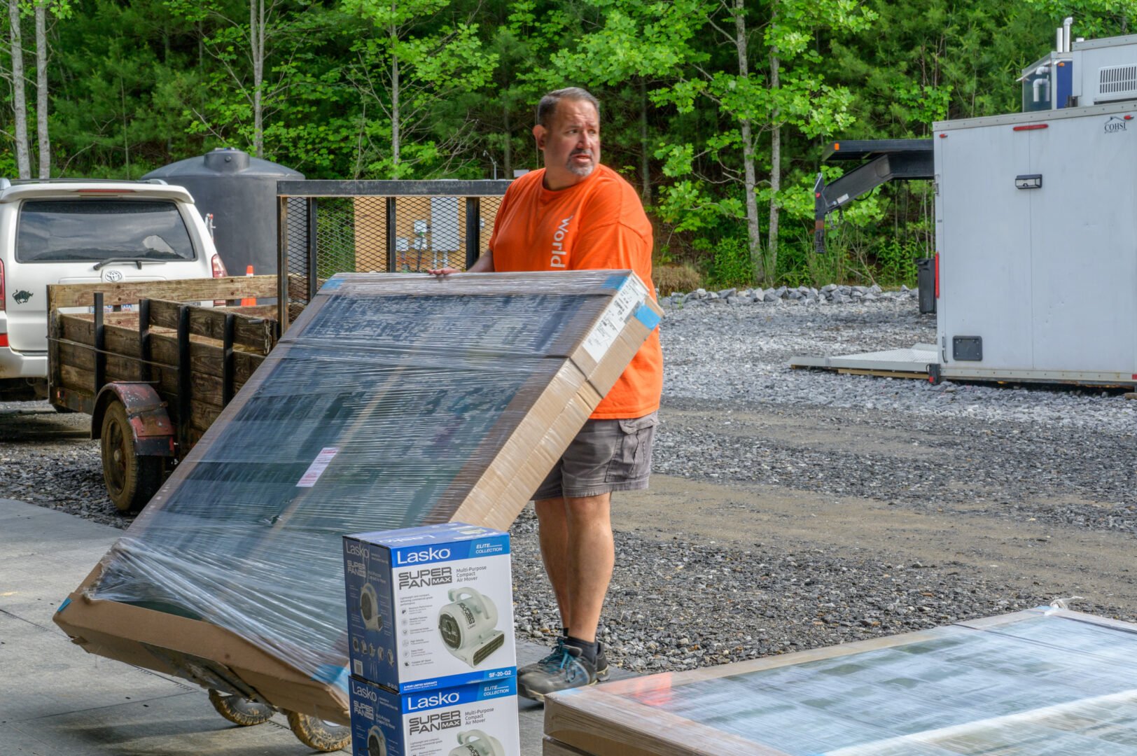 Man wearing an orange shirt with World Vision written on it pulls a plastic-wrapped window on a dolly.