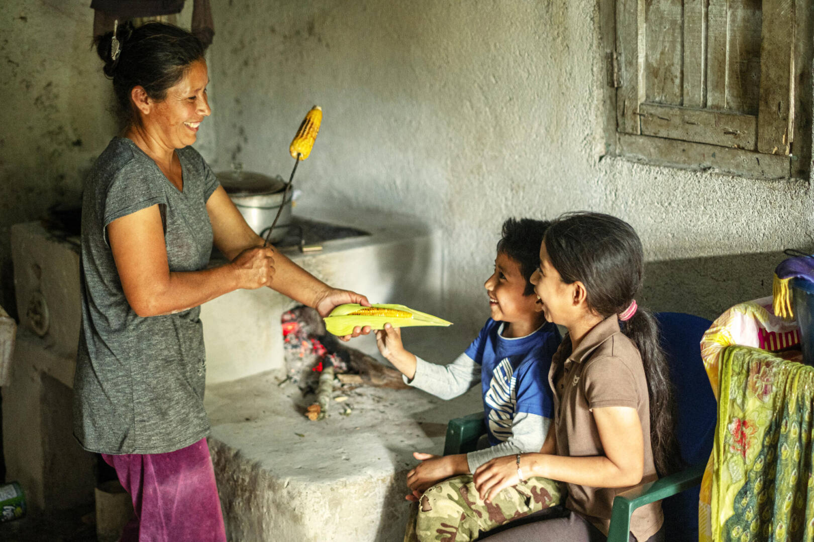 María and children A mother hands her two children a stalk of roasted maize to share.
