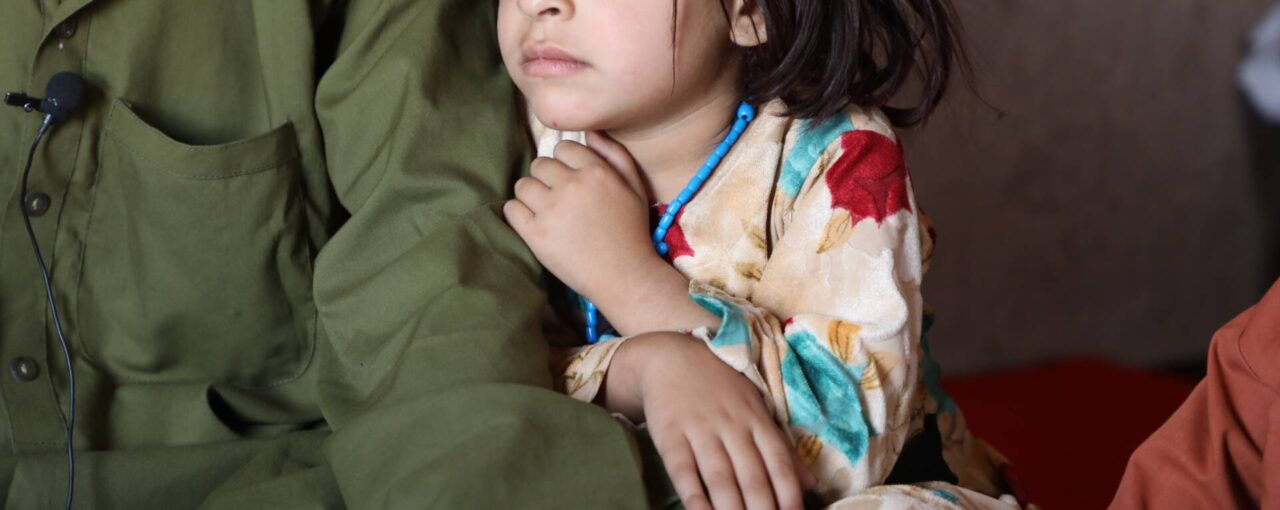 Maryam, seen from the nose down, sits near her father, whose face is not shown.