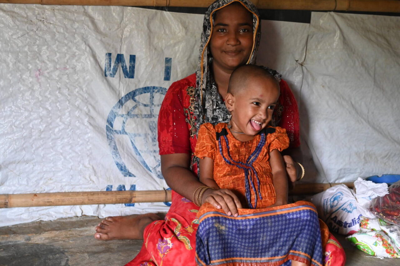 Mother and daughter in Cox’s Bazar A young Rohingya girl sits on her mother’s lap, smiling.