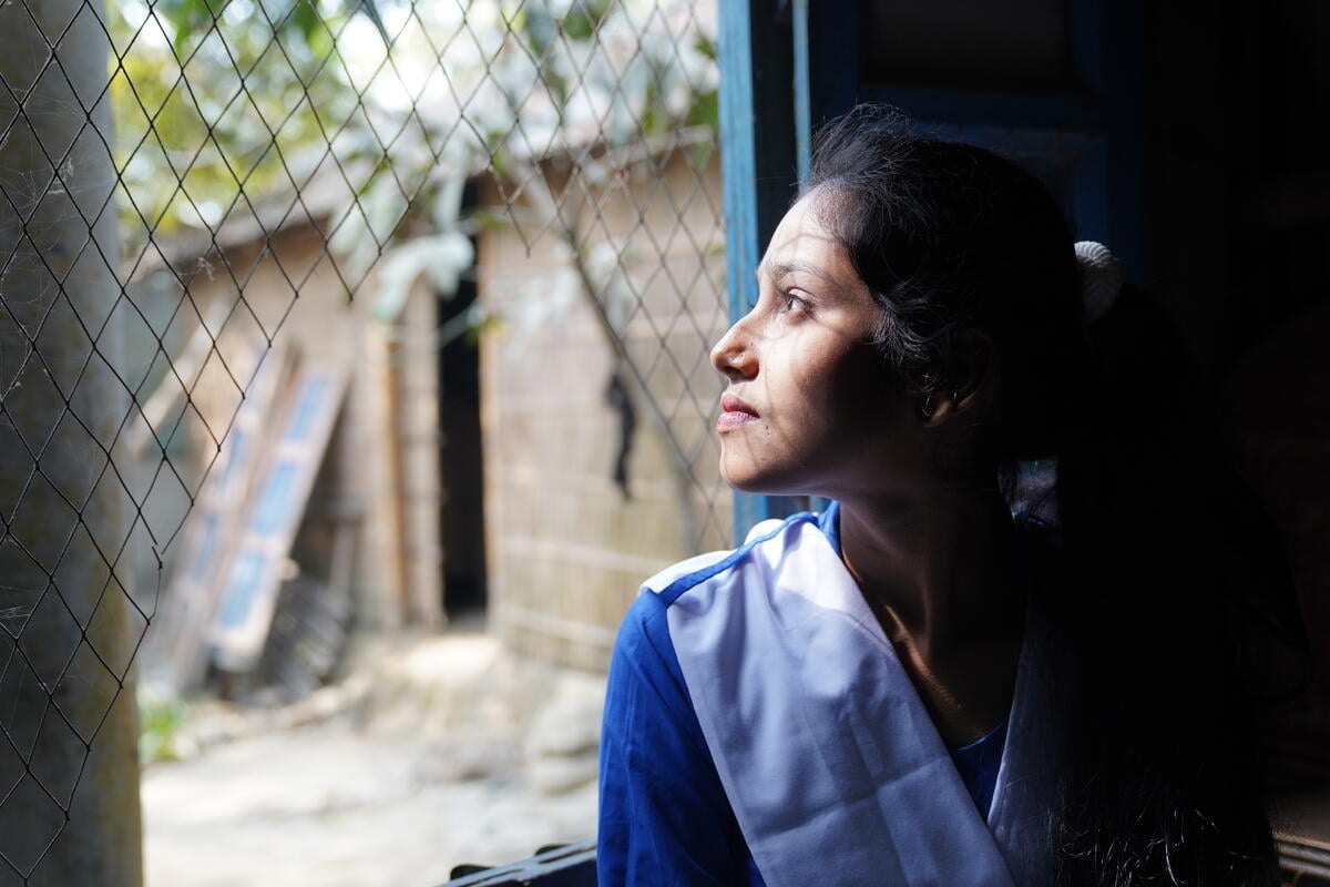 A girl with a somber expression stares out a window.