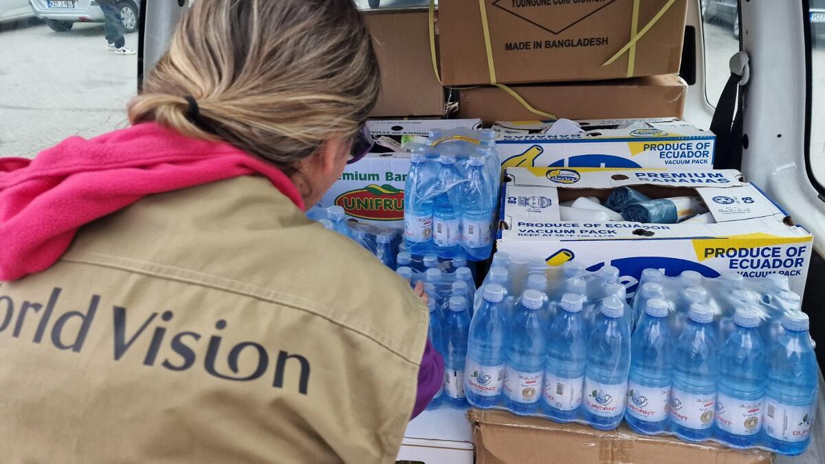 An aid worker oversees packaged bottled water and boxes filled with hygiene supplies.