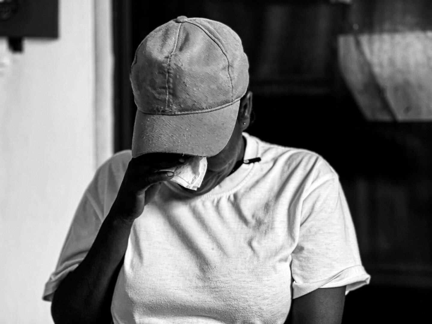 A black-and-white image of a woman with her head down, holding a tissue to her face, appearing reflective and emotional.