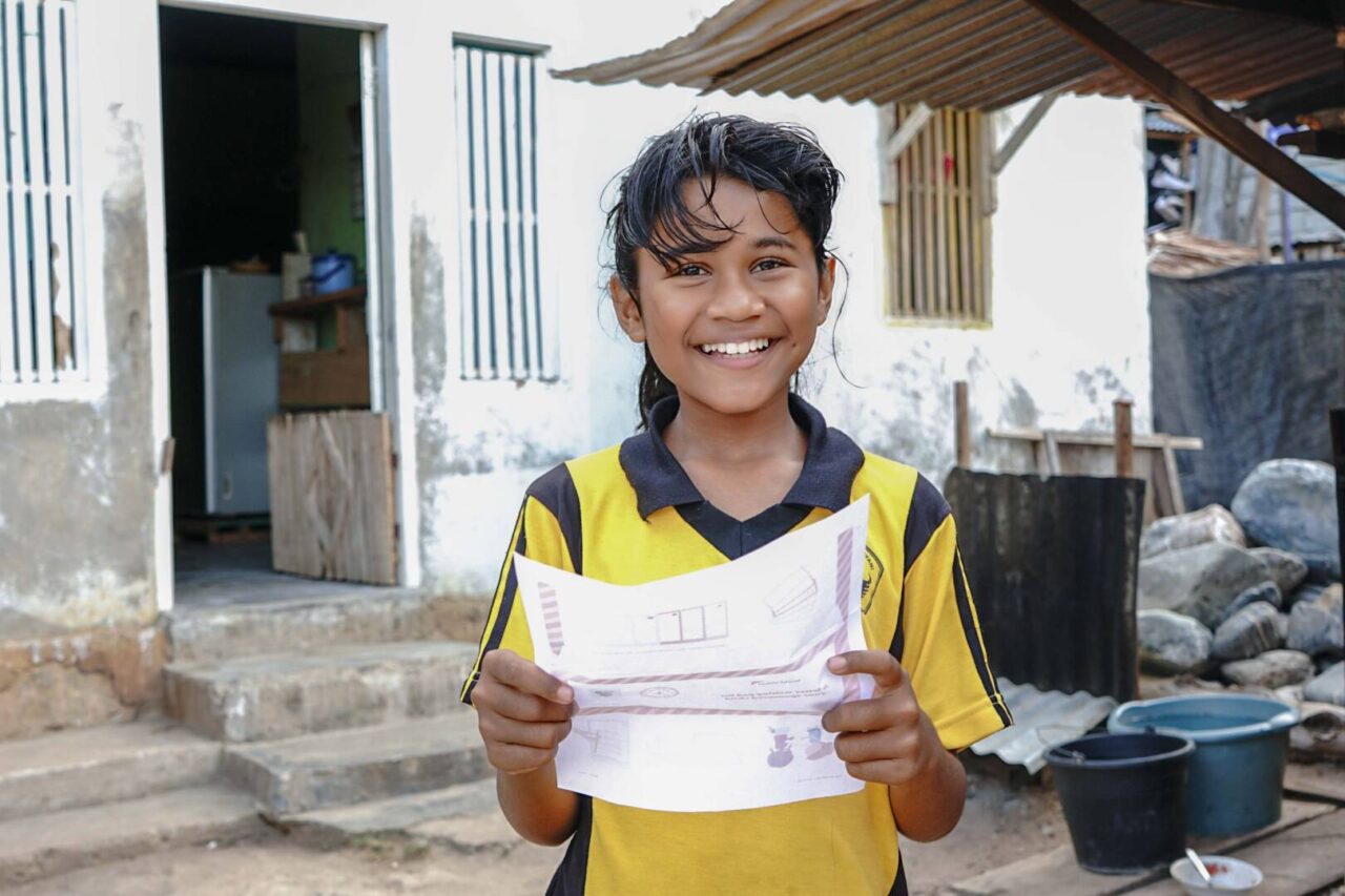 Sponsored child with letter Rahmawati, 10, in Indonesia is excited to get a letter from her World Vision sponsor. A smiling girl in a yellow shirt holds a letter.