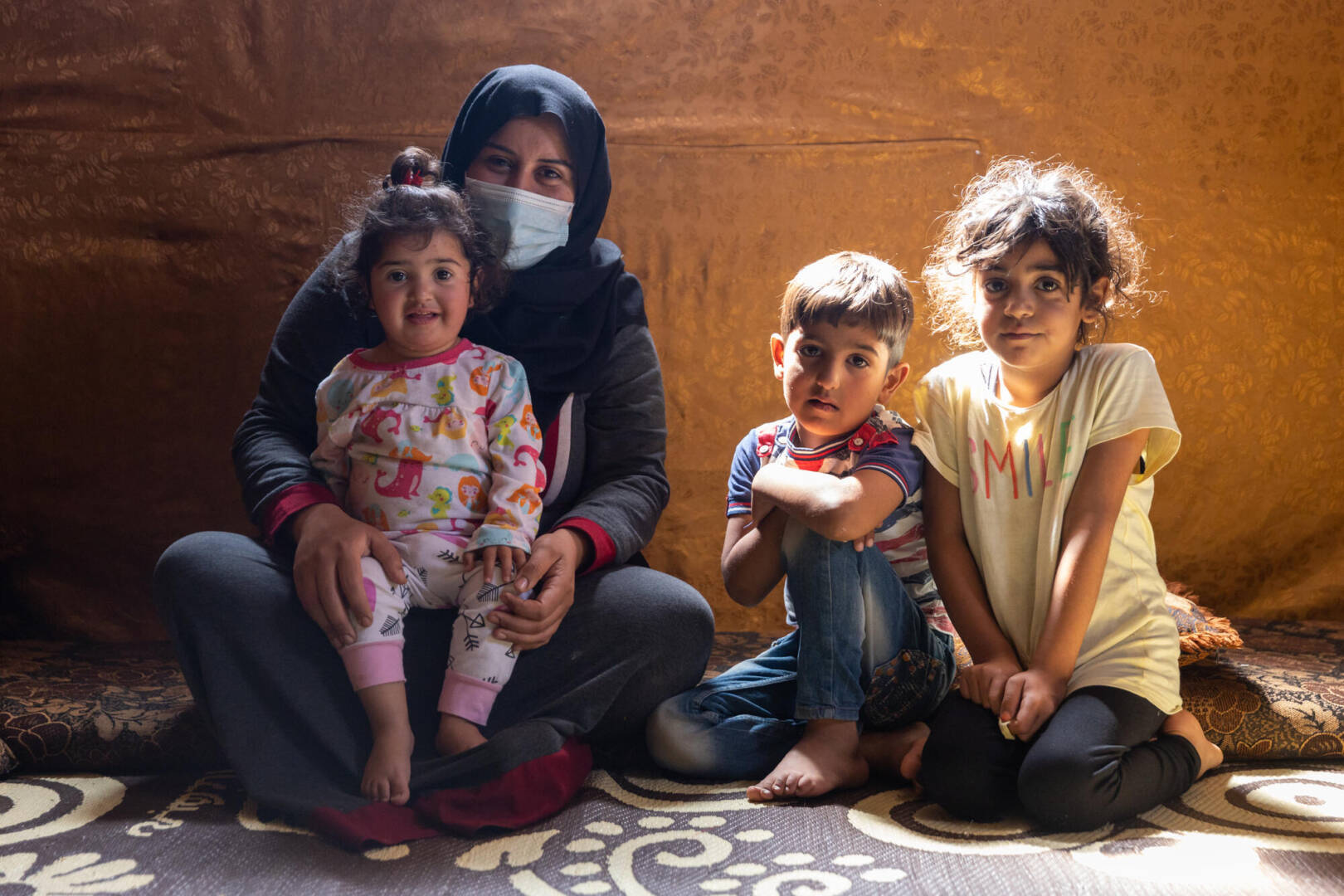 Abir and family Abir and her three children look toward the camera in an informal settlement in Lebanon