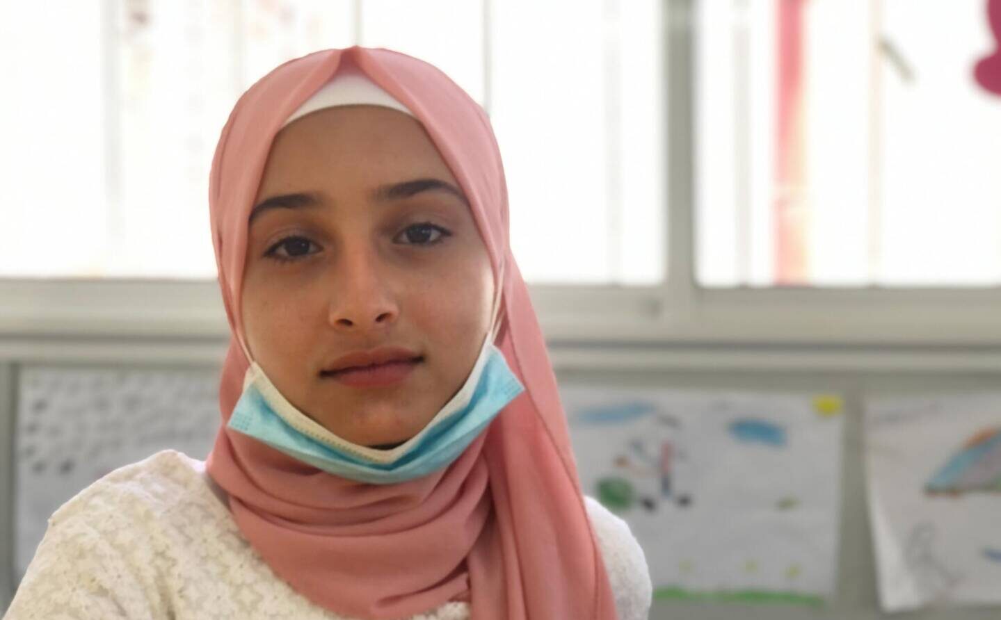 A light pink headscarf frames Imane&rsquo;s face as she looks at the camera in a World Vision Child-Friendly Space.