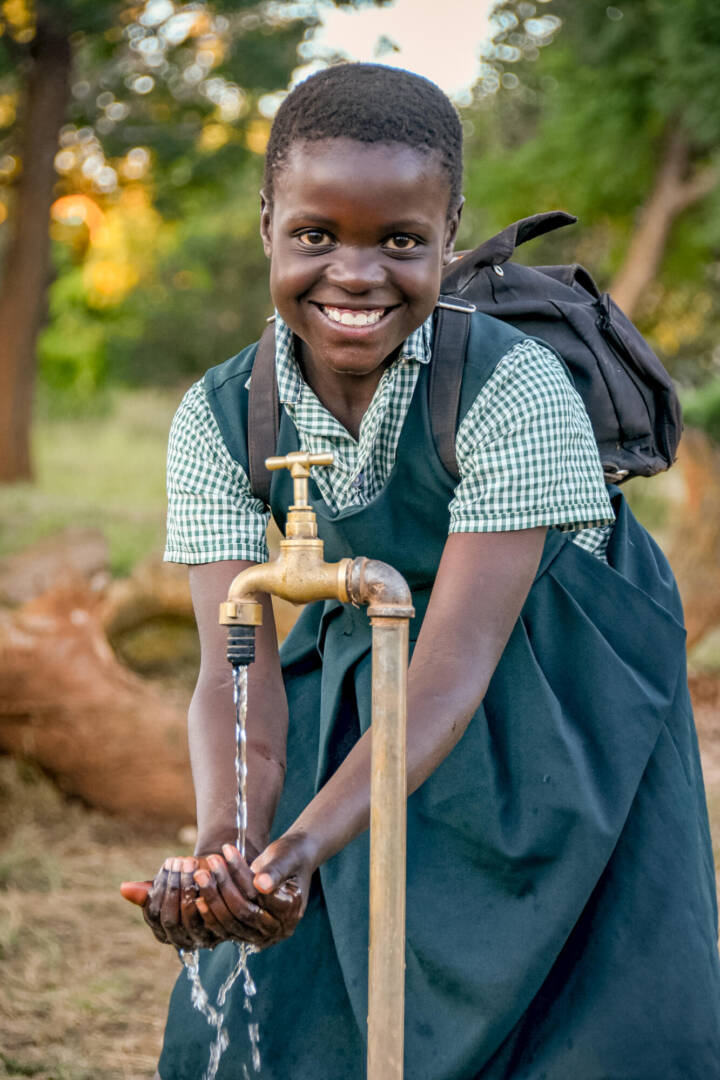 With a water tap installed by World Vision, water pours into Juliet’s hands.