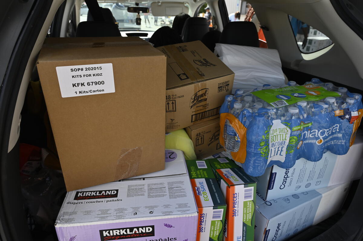 Bottled water, Lysol cleaning supplies, and other relief items are stacked inside the back of a vehicle.